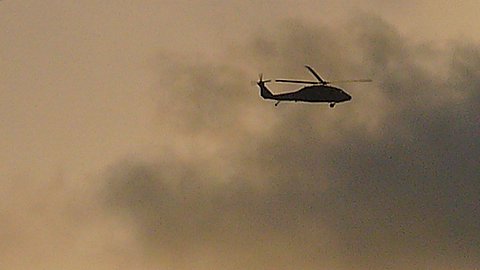 an army helicopter flying through a cloudy sky