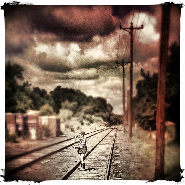 a person walking down a train track with clouds above