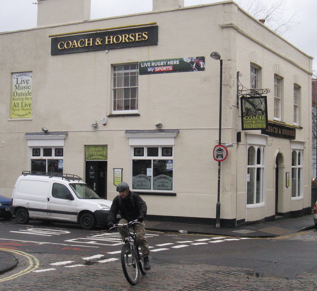 man on bike in front of a business called coach and horses