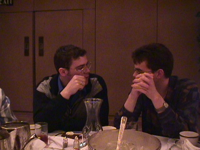 two men sitting at a table eating food