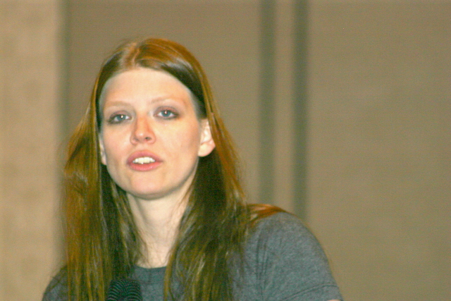 a woman is wearing a grey top while she has long brown hair and blue eyes