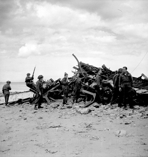military men looking at wrecked vehicles on a beach