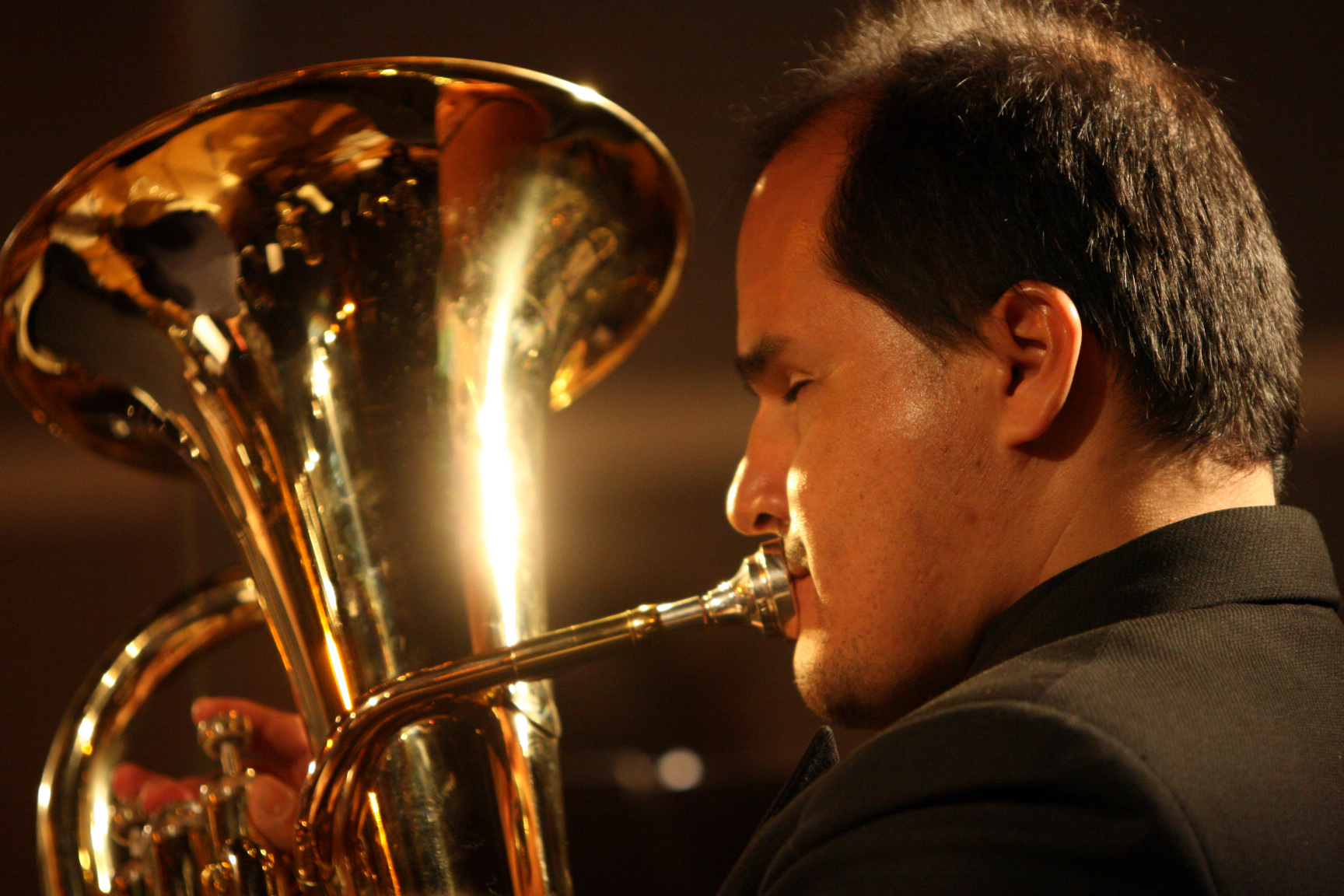 a man with black hair in a dark suit and gold trumpet