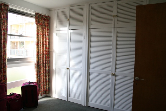 a bedroom with white shutters and a red suitcase