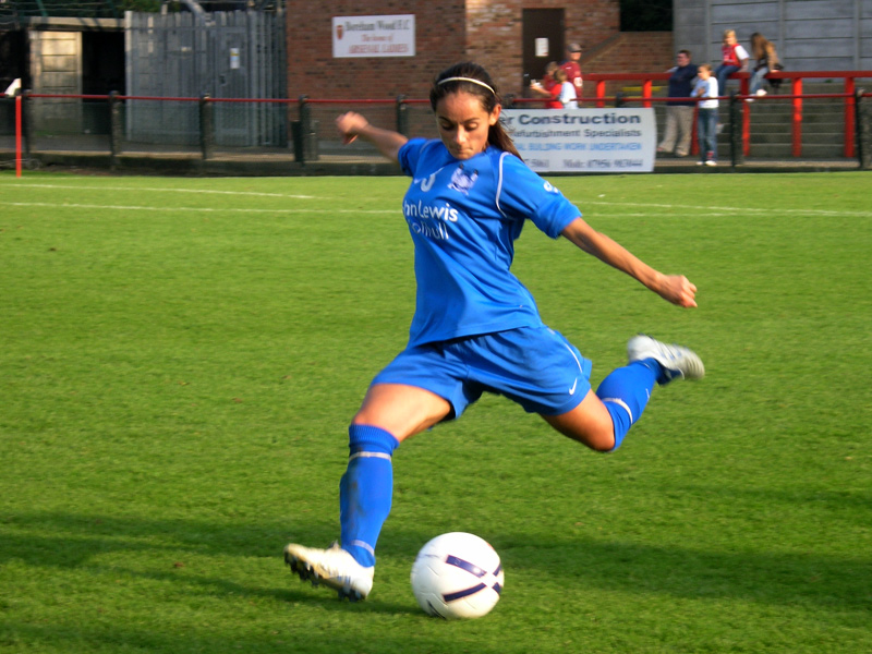 a girl in blue kicks a soccer ball on the field