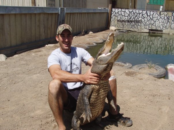 a man sits on the ground holding an alligator