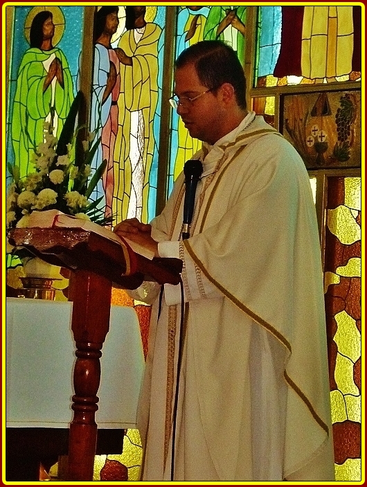 priest reading a bible in front of stained glass windows
