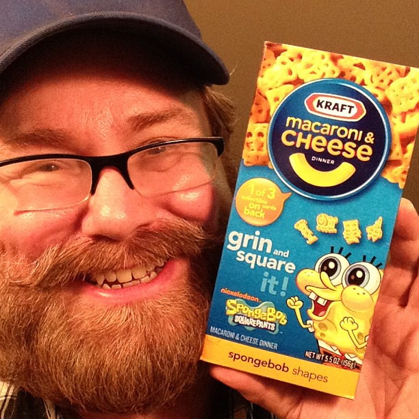 a man with beard holding up a box of macaroni cheese