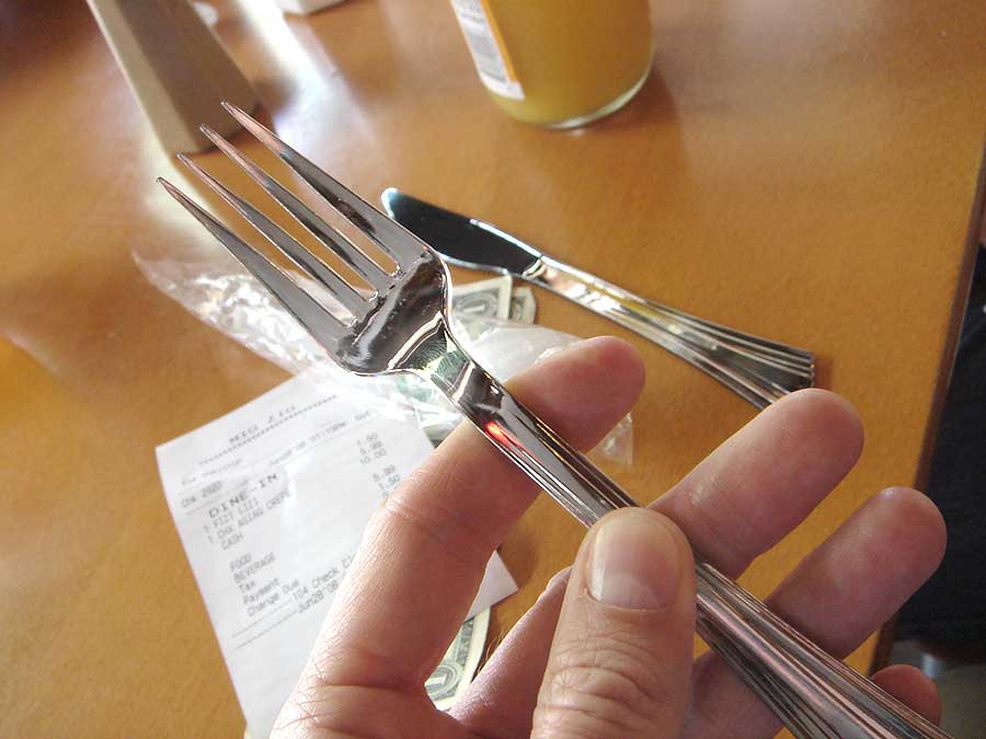 a hand holding three forks over a wooden table