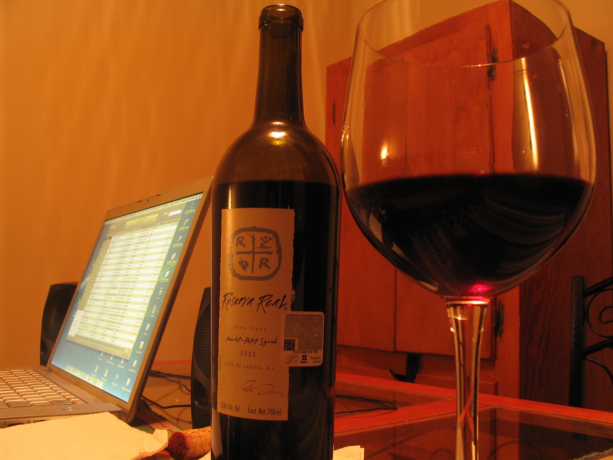 a bottle and glass of wine with a laptop on the desk in the background