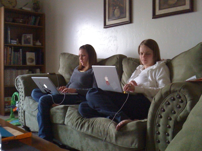 two s sitting on a couch with laptops in their hands