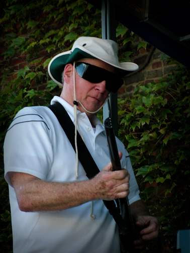 a man wearing suspenders holding up a rifle with a hat on it