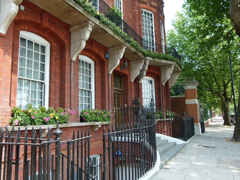 row of brick buildings and wrought iron fences in front of trees