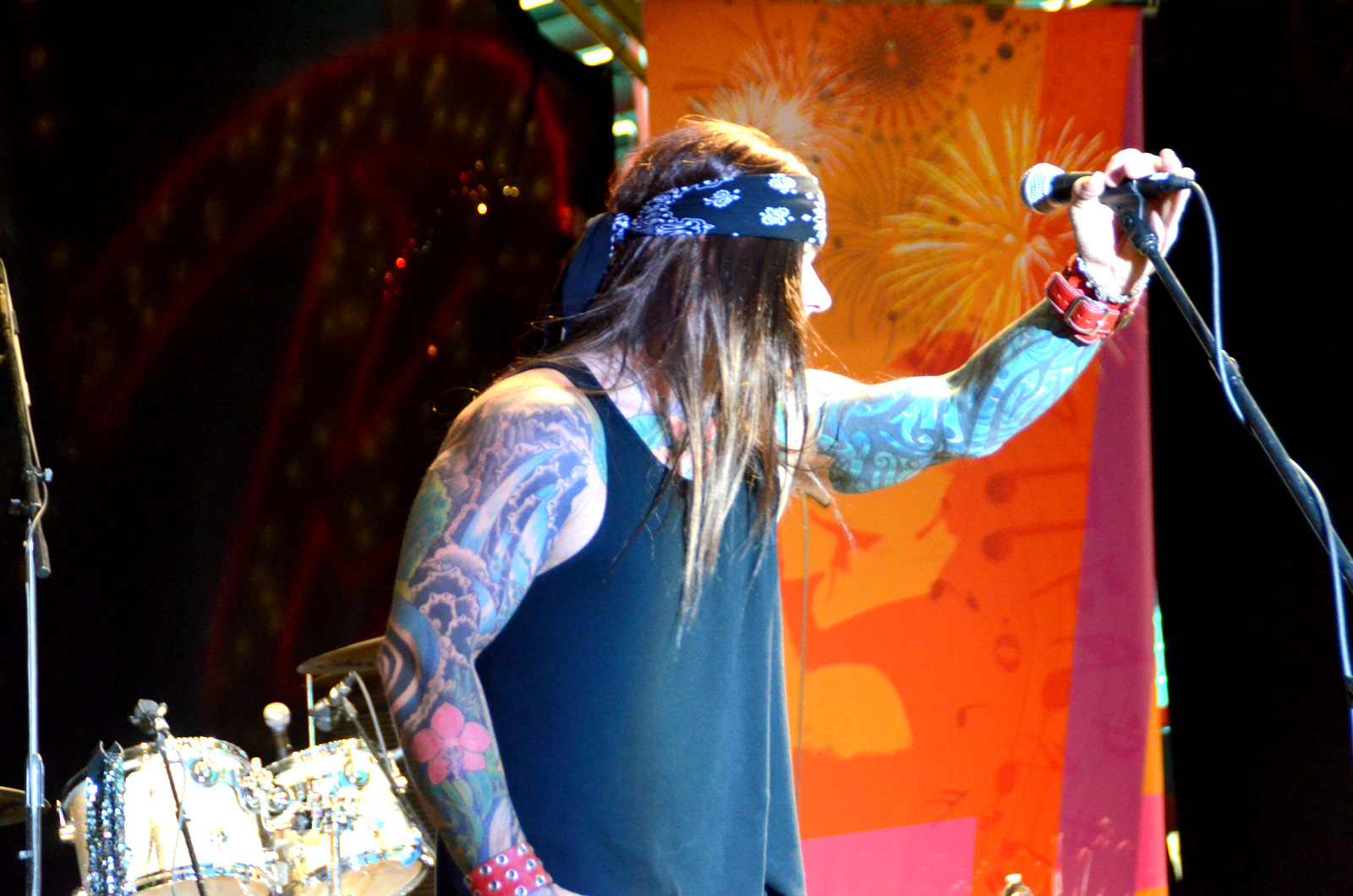 a musician with long hair holding a microphone and wearing a bandana