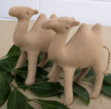 three small stuffed camels sitting next to green leaves