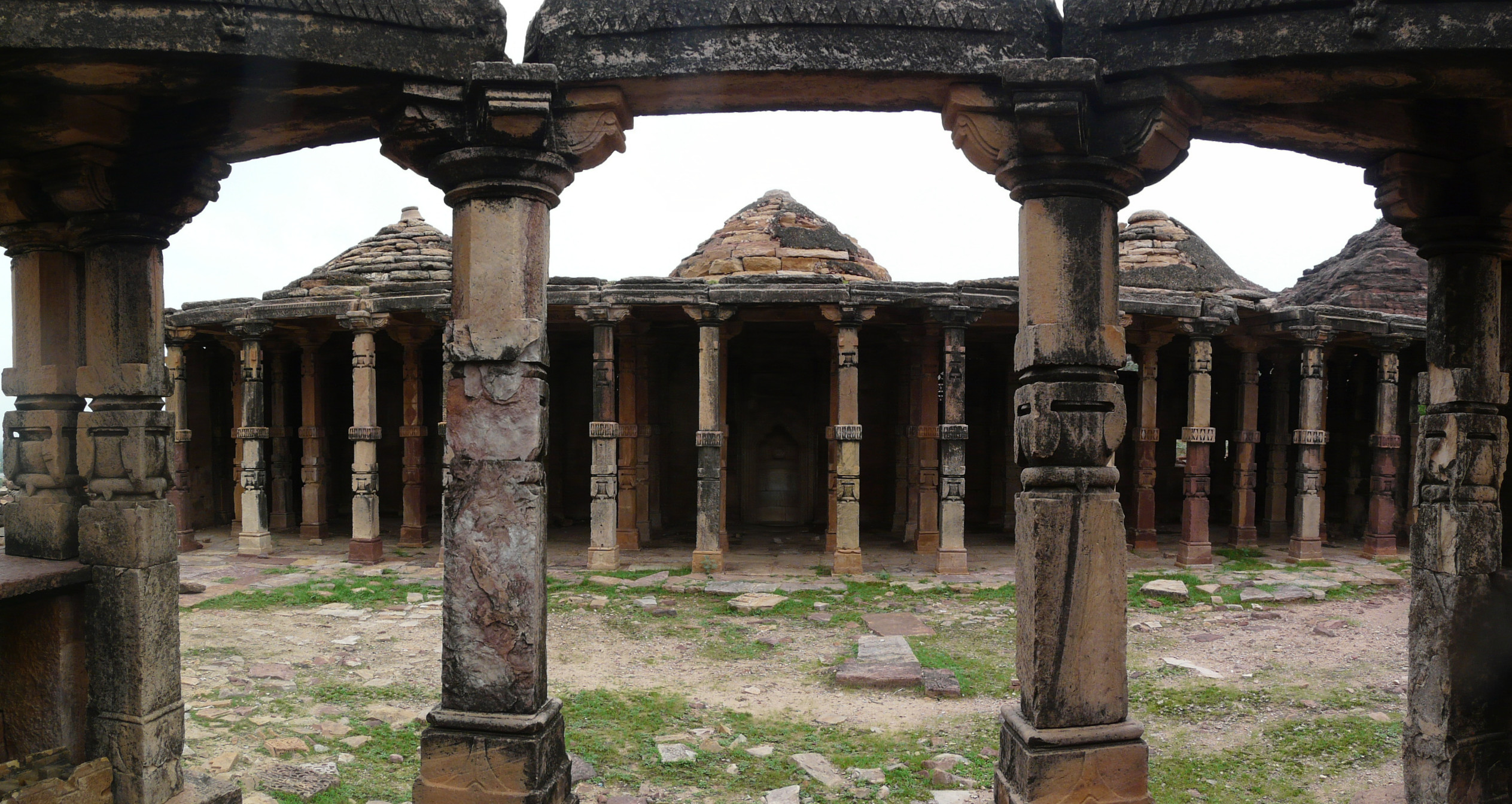 a bunch of columns in the dirt near some buildings