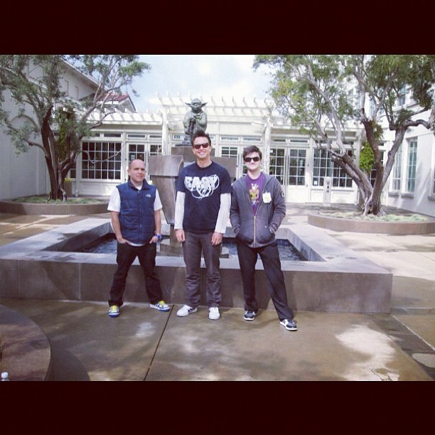 three men standing outside with each other in front of a fountain