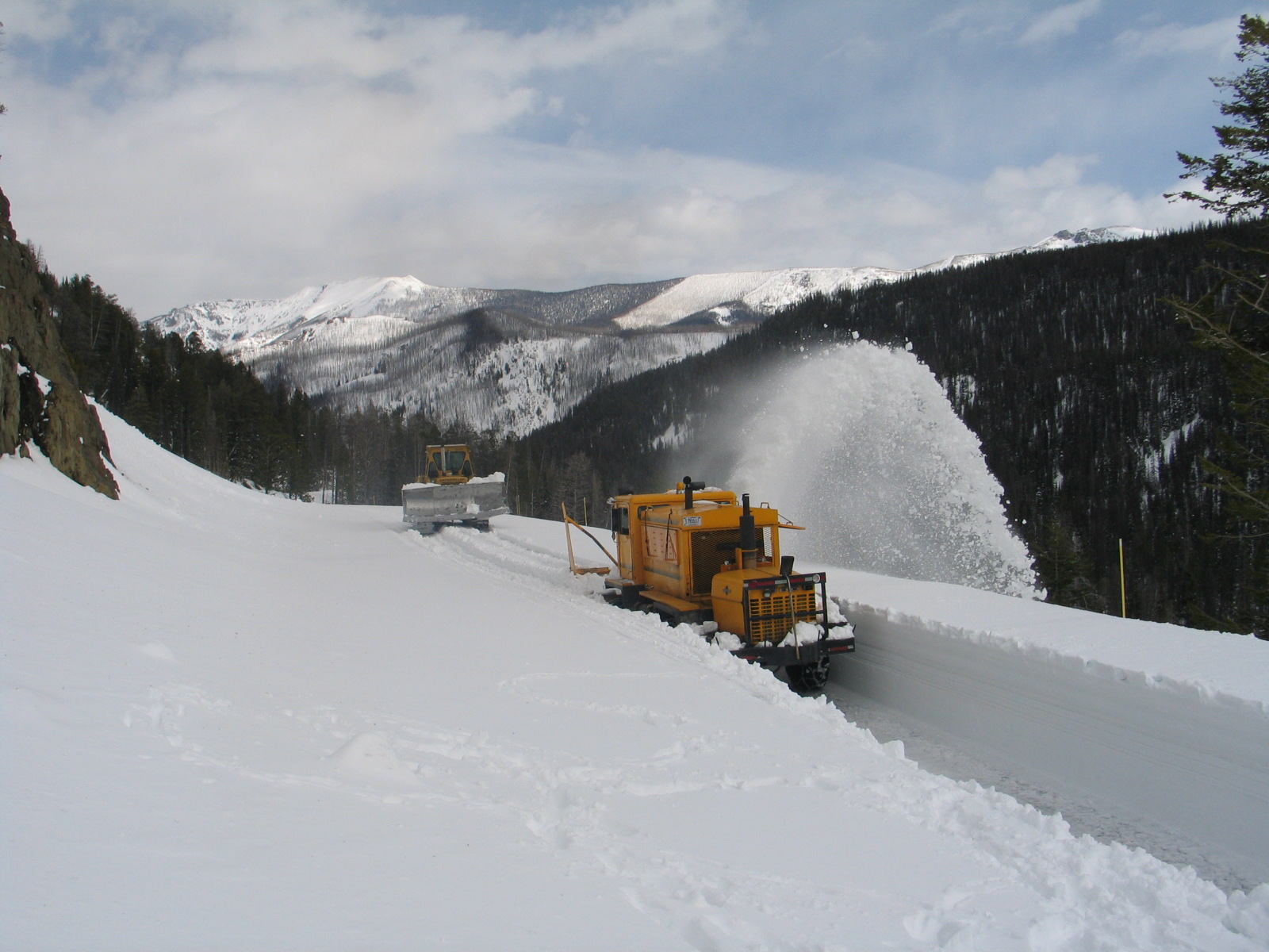 two snowplows are in the snow near a large snowy mountain