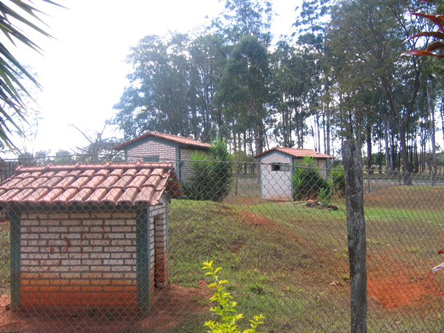 a red brick building near a forest behind a chain link fence