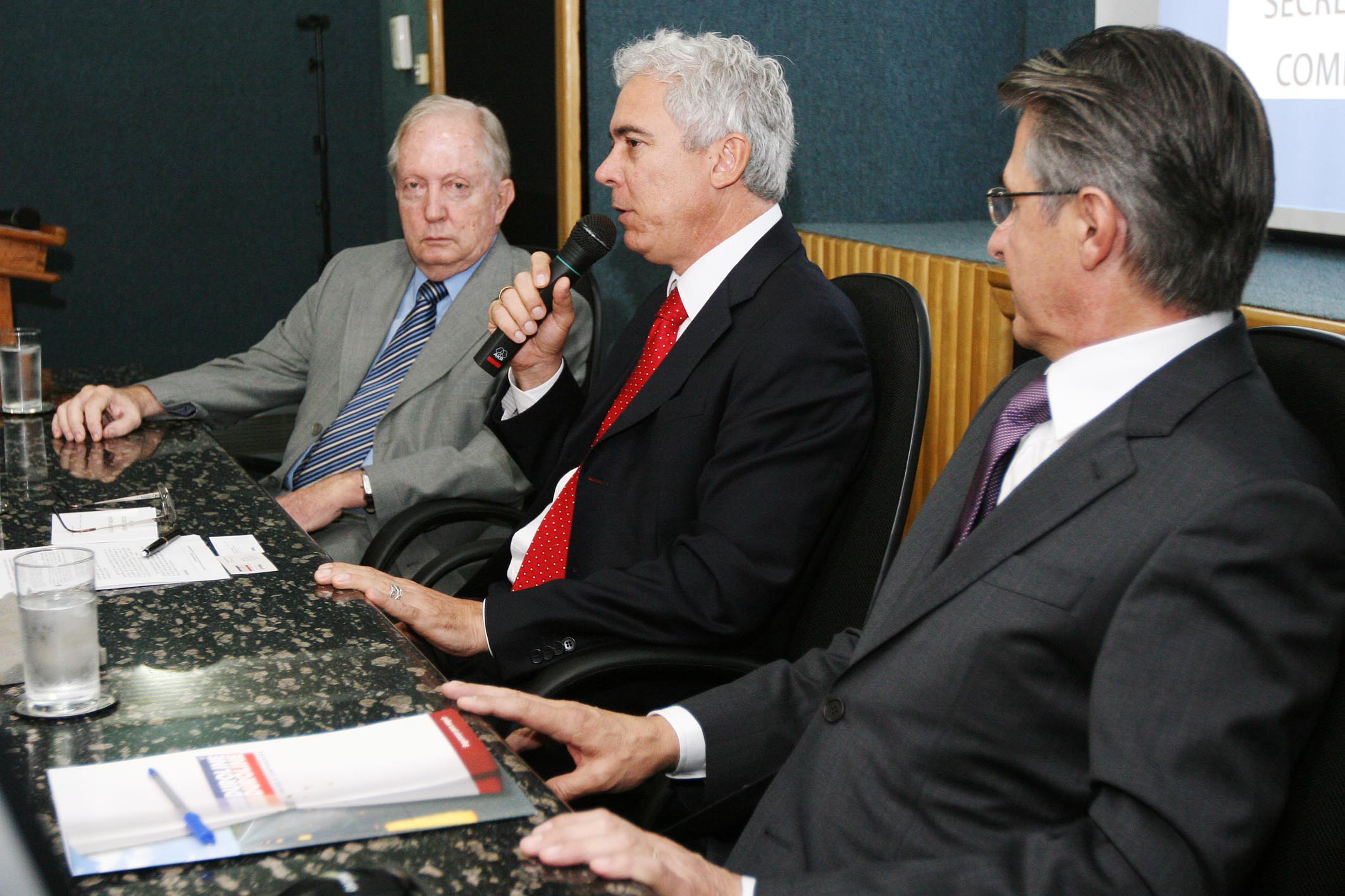 four men seated at a table with microphones and books