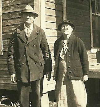 an old man standing next to a woman near a cabin