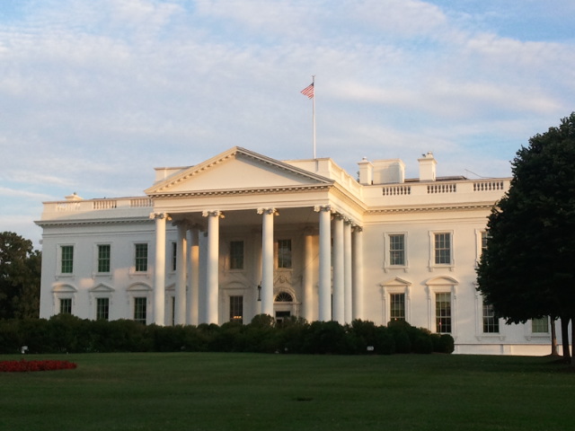 the white house with trees and shrubs surrounding it