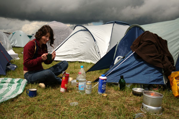 a woman sitting next to several tents with bottles and cans