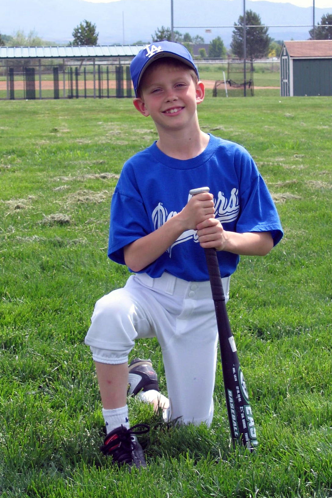 a boy in blue uniform with baseball bat and glove