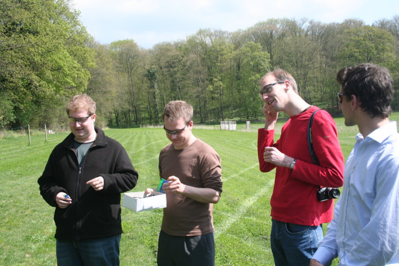 four men standing on a field checking their phones