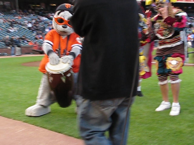 a mascot is playing drums with a  on the other side of the stadium