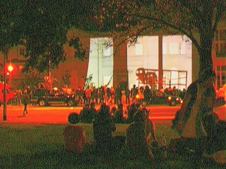 a group of people walking along the sidewalk at night