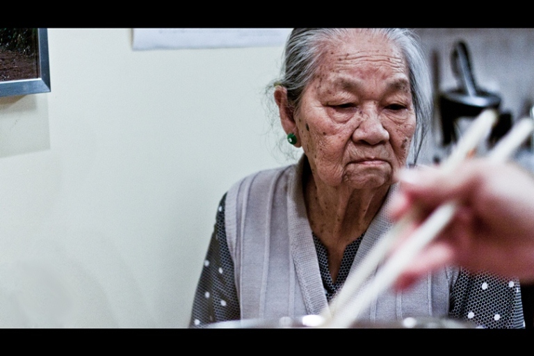 an old woman eats rice with chopsticks