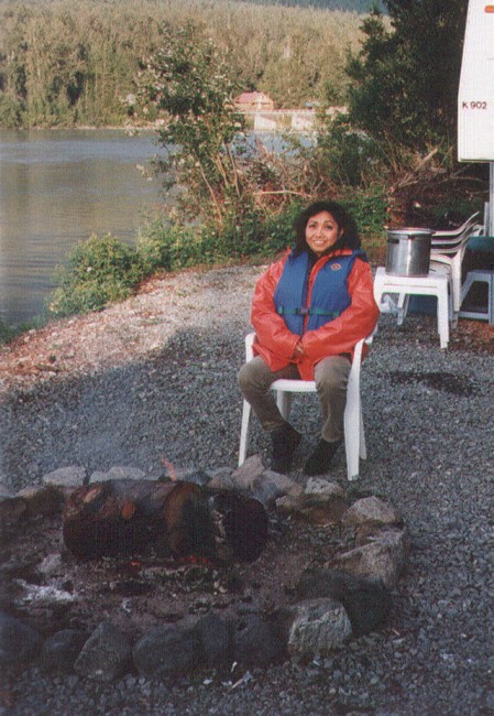 a woman is sitting next to a camp fire in her campsite