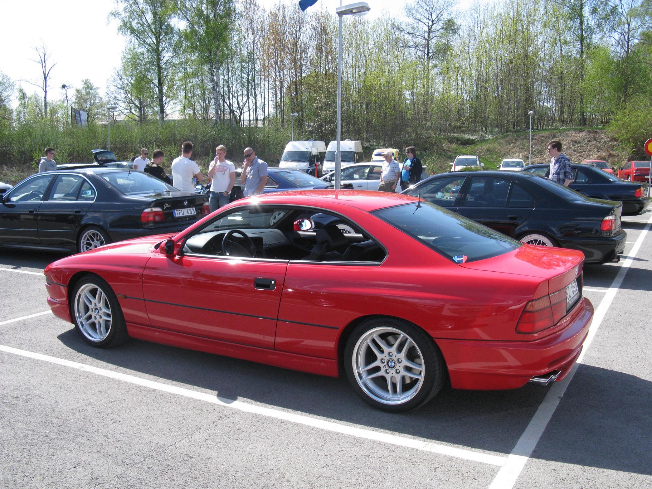 an orange car parked in a lot with a group of people looking at it