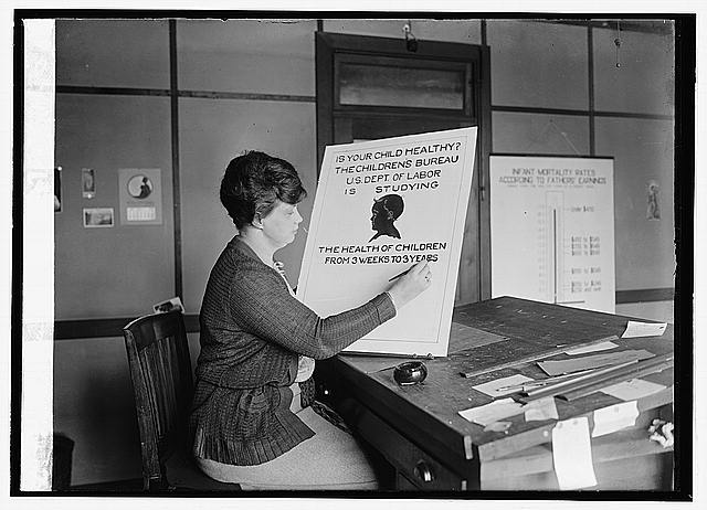 an old po shows a woman standing at a desk and reading