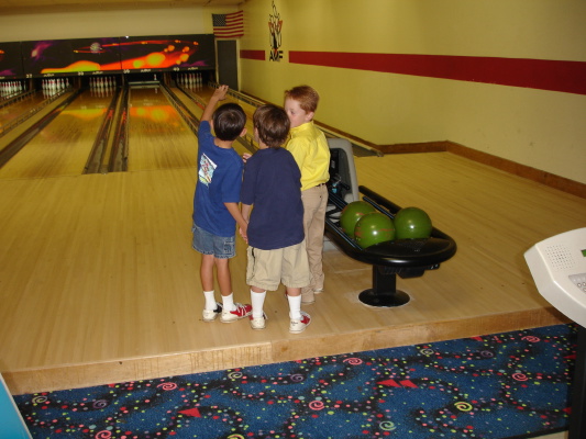three children are in a bowling alley looking at a green ball