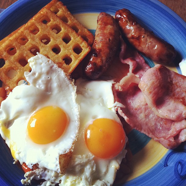 two eggs, sausage, waffles and bacon sit on a blue plate