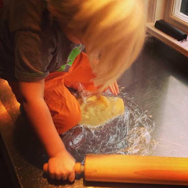 a child rolling dough on a baking sheet and an orange apron