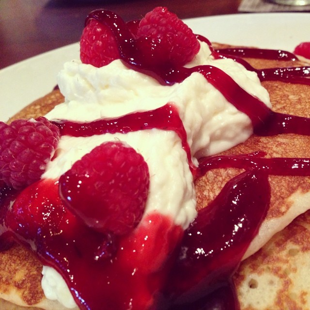 closeup image of a stack of pancakes with whipped cream and raspberries