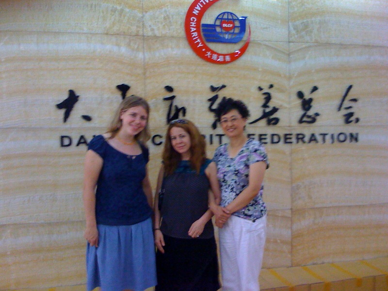 three women are posing by a wooden sign