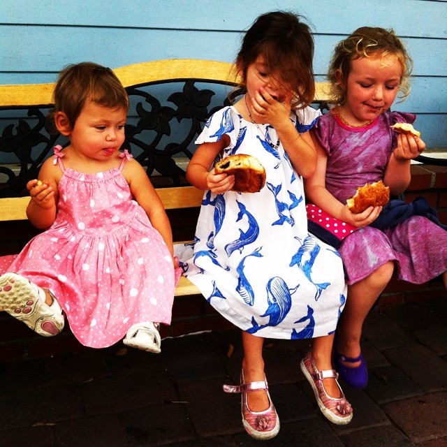 three little girls sit on a bench with their mouths open