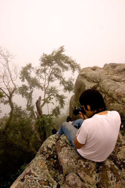 a man sits on a rocky ledge and takes a po