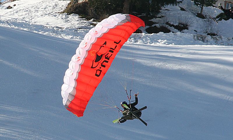 a man is skiing and holding onto an orange parachute