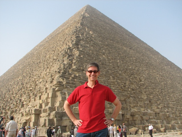 a man in a red shirt standing in front of a tall pyramid