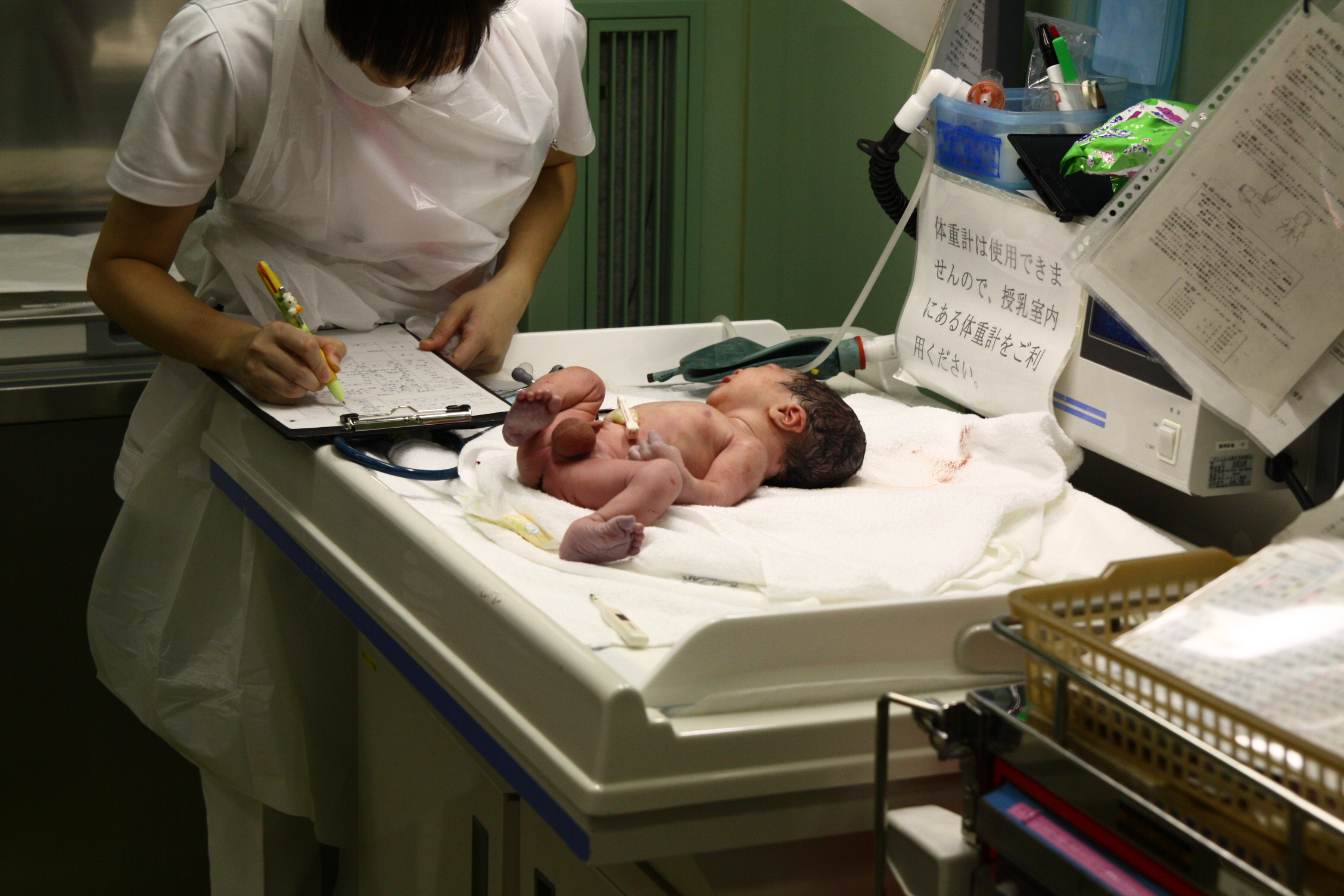 a woman in white uniform standing over a baby laying on a hospital bed