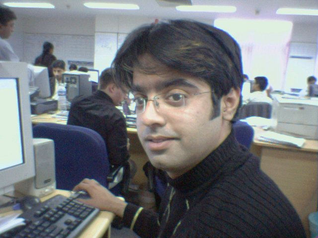 a man wearing glasses at a computer looking at the camera