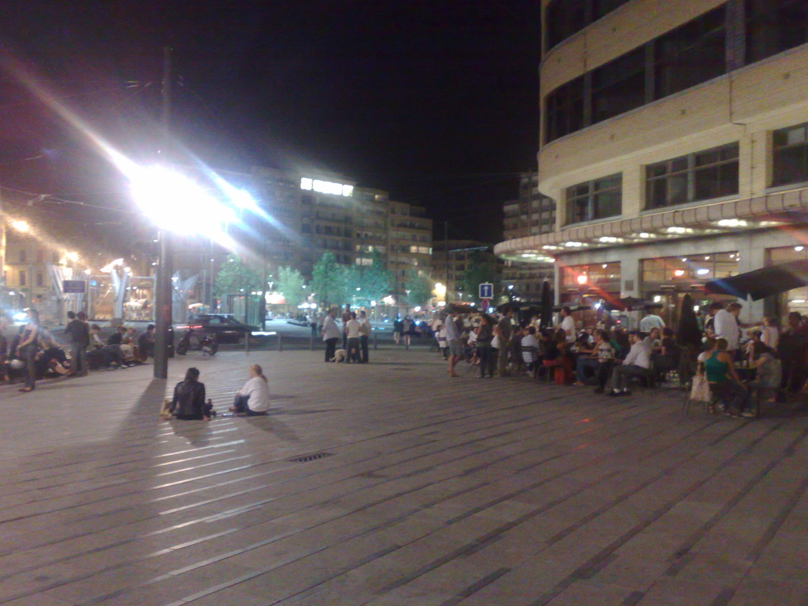 people are sitting and standing in a large square at night