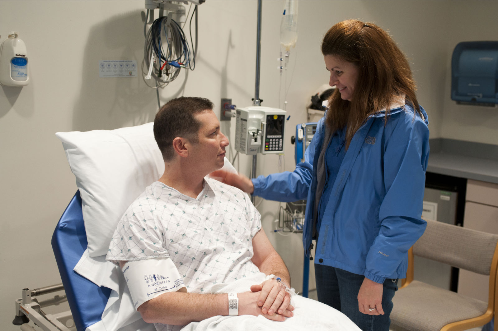 a man in a hospital bed talking to a woman who is holding his hand