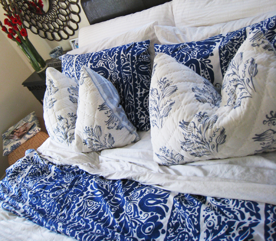 blue and white pillows on a bed with a mirror above