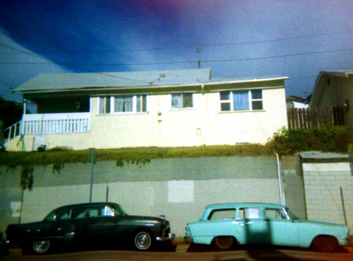 old cars sit on the sidewalk in front of a two story house